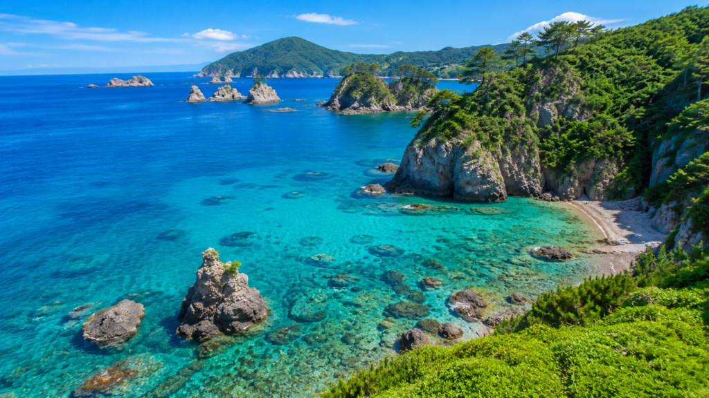 Crystal-clear blue sea with rocky coves and lush green cliffs along the Japanese coast